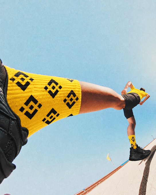 Two people wearing matching yellow socks with a black geometric pattern and black shoes, posed playfully against a blue sky.
