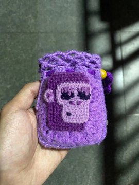 A hand holding a small purple crocheted pouch featuring a pixelated character design, likely representing one of the Krypto Chay NFTs.
