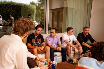 A group of casually dressed individuals sit together outdoors on a patio, engaged in conversation, with drinks visible on the table in front of them. The relaxed gathering reflects the post's sentiment of a casual meeting with OKX representatives, likely following a discussion or collaboration between the host and the crypto exchange team.