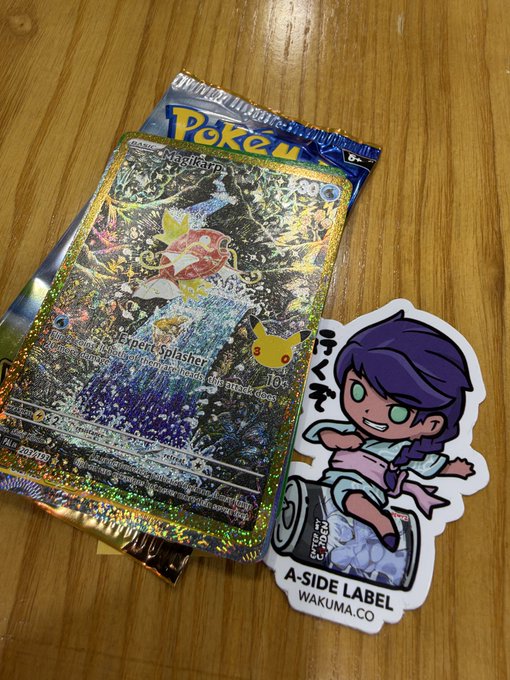 A holographic Pokémon trading card, appearing to be a Pikachu ex, lies on a wooden surface next to a sticker of a purple-haired anime character labeled 'A-SIDE LABEL WAKUMA.CO'.