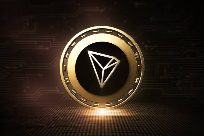 A golden TRON (TRX) cryptocurrency coin with its triangular logo on a dark circuit board background.