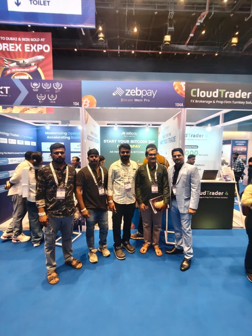 A group of six men posing at a trade expo booth for ZebPay and CloudTrader, with banners reading 'Bitcoin Mein Pro' and 'Start Your Bitcoin Journey Today' at a forex/crypto event.