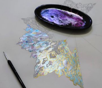 An artist's desk showing a work-in-progress painting of an iridescent golden and blue crystalline butterfly-like form on paper, alongside a black oval palette with purple paint.