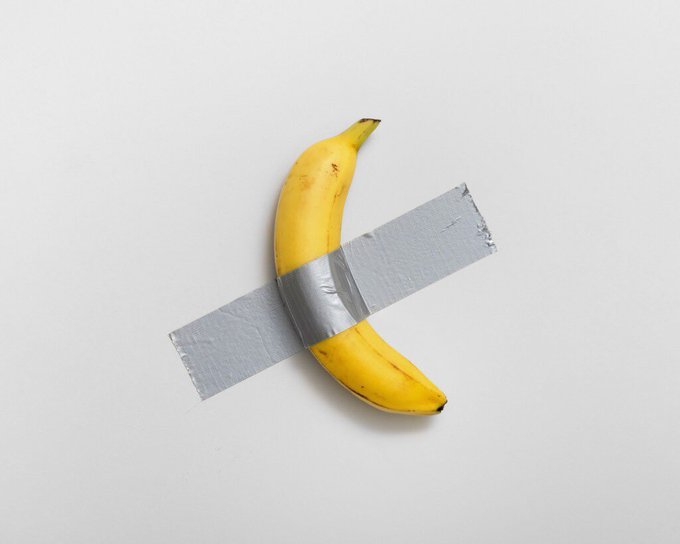 A yellow banana taped to a white wall with a single strip of silver duct tape, referencing the conceptual artwork 'Comedian' by Maurizio Cattelan.