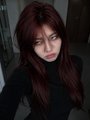 A portrait of a person with long dark hair and red lipstick wearing a black top.