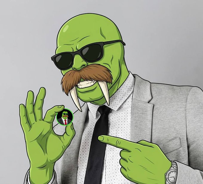 A green-skinned cartoon character wearing sunglasses, a grey suit, and tie makes an OK gesture while holding a small circular pin featuring a suited figure.