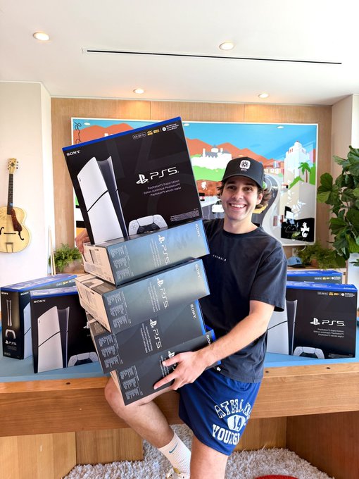A smiling young man in a black cap and shorts sits holding a tall stack of PlayStation 5 (PS5) boxes, with more PS5 consoles lined up on the wooden table behind him and a colorful Sonic-themed mural on the wall. The image promotes a giveaway by @earnos_io offering 10 PS5 consoles paired with GTA 6 Standard Edition pre-orders.