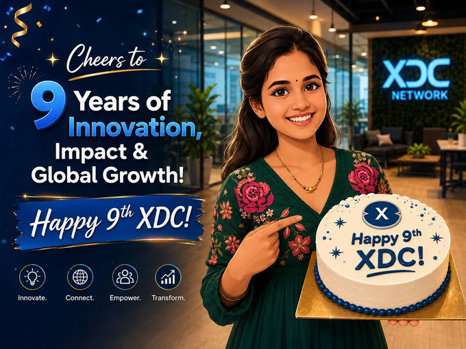 The main focus of this image is a woman standing next to a large cake decorated with blue and white frosting flowers holding up her left hand while pointing at the cake. The backdrop features a festive banner celebrating the 9th anniversary of XDC Network, which includes "Happy 9th XDC!", "#XDC", and the company's name written in pink and blue text on it.