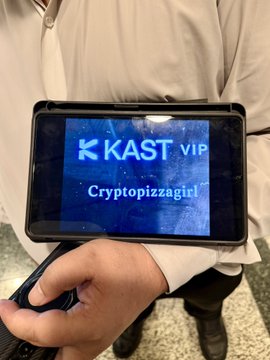 A close-up of a smartphone screen displaying the "KAST VIP" logo with the username "Cryptopizzagirl," held by a traveler who just arrived in Singapore and received a free ride from KAST. The screen aligns with the post's context of using KAST's services upon landing.