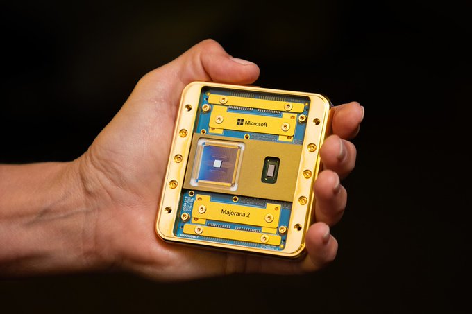 A hand displays Microsoft's Majorana 2 quantum chip, featuring a gold-colored casing with visible internal components labeled "Microsoft" and "Majorana 2," representing the company's controversial topological qubit technology that is now being made available to DARPA for independent testing.