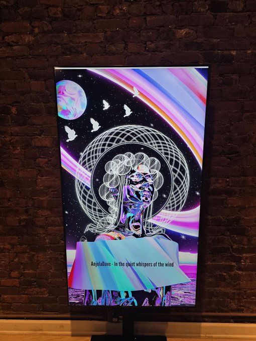 A monitor displaying vibrant, psychedelic digital art of a face with rainbow light streams and doves, titled 'AnjetaDave - In the quiet whispers of the wind'.