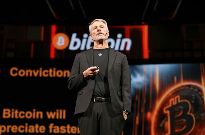 Michael Saylor, executive chairman of Strategy, speaks at a Bitcoin conference, with the Bitcoin logo and text "Bitcoin will appreciate faster" and "Conviction" visible on screens behind him—tying directly to the post's highlight that Strategy alone holds the vast majority of public-company Bitcoin treasuries.