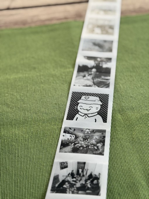A strip of black-and-white film prints, including one with a cartoon character wearing a heart cap, lies on a green textured surface.