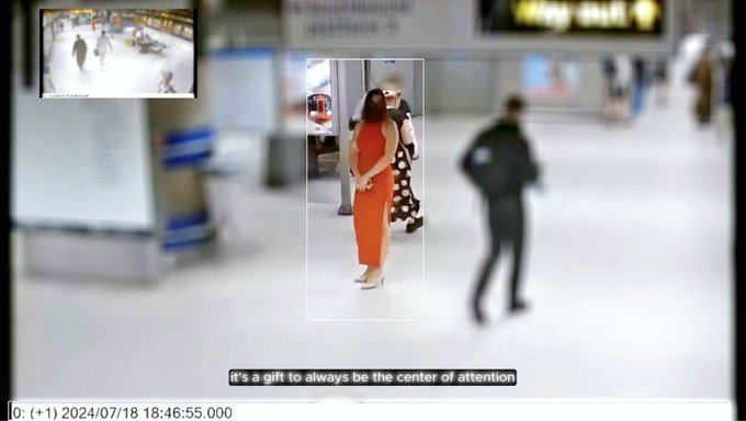 CCTV footage showing a woman in an orange outfit walking through an indoor public space, with subtitles reading 'it's a gift to always be the center of attention'.