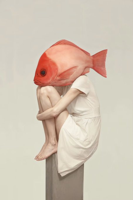 A person in a worn white dress sits hunched on a stone pedestal, their head replaced by that of a red fish, evoking a quiet, melancholic isolation. The artwork's emotional weight matches its title, with the muted tones and withdrawn pose capturing a sense of vulnerability and introspection.