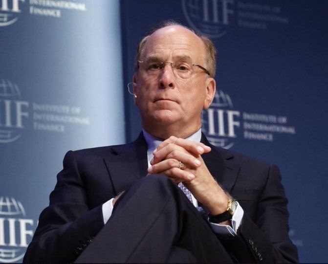 A man in a dark suit and glasses sits attentively with his hands clasped, set against a backdrop featuring the "IIF Institute of International Finance" logo, suggesting his appearance at a financial panel in response to major Bitcoin ETF sell-offs totaling $144.6 million from firms like BlackRock and Fidelity.