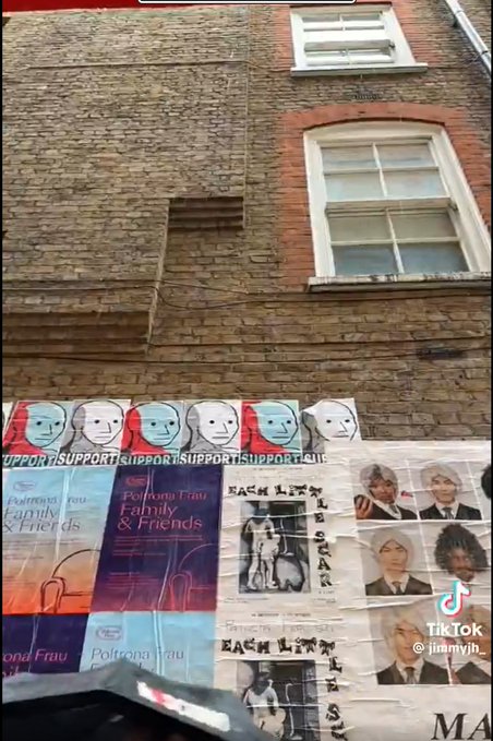 A brick building wall with windows above and a collection of posters below, including repeated 'SUPPORT' banners with cartoon faces, 'Poltrona Frau Family & Friends' advertisements, and anime character posters. The TikTok watermark shows @jinmyjih.