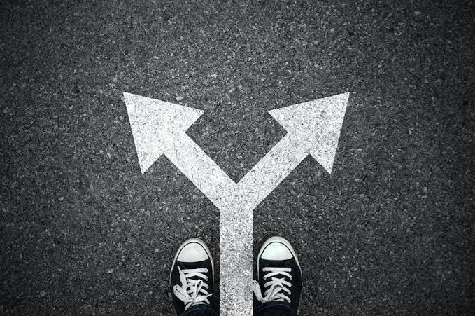 A person stands at a crossroads on asphalt, with one arrow pointing left and another right beneath their sneakers, symbolizing a pivotal decision or fork in the road—mirroring the post's message about an upcoming "pivot race" between L1 and L2 chains like Sophon and Polygon.