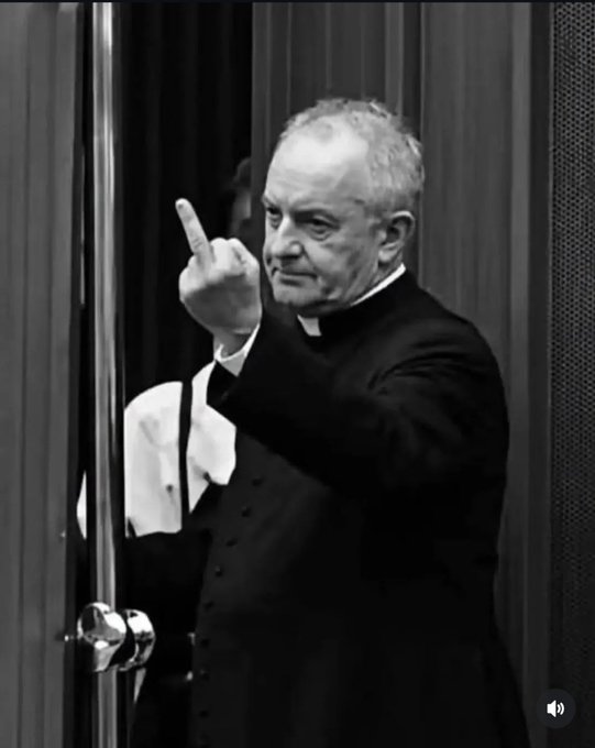 A black-and-white image shows a stern man in formal clerical-looking attire raising one finger while entering through a doorway.