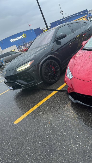 A black Lamborghini Urus parked next to a red sports car in a wet Walmart parking lot.