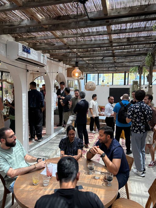 A group of people gather at an indoor-outdoor venue with a wooden ceiling and woven lighting fixtures, seated around a circular table having drinks and conversation during what appears to be a networking lunch event.

The caption context note confirms the gathering is a Solana-hosted lunch event, which aligns with the image showing attendees engaged in discussion and networking typical of a crypto/web3 industry meetup.