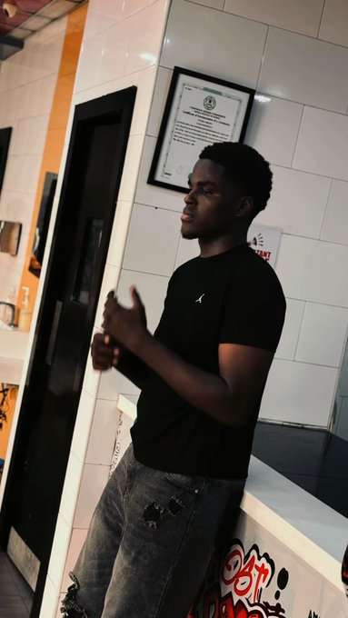 A young man in a black t-shirt and distressed jeans stands with his eyes closed and hands clasped together in a prayer-like gesture in front of a counter, seemingly making a wish or expressing hope. The pose matches the post's plea to "bag the ansem airdrop," as if he's manifesting a successful crypto airdrop.