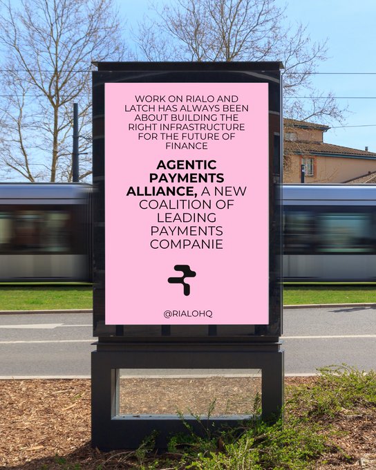 An outdoor advertisement billboard with a pink background displays text about Rialo and Latch building infrastructure for the future of finance, along with the Agentic Payments Alliance logo and the handle @RIALOHQ.