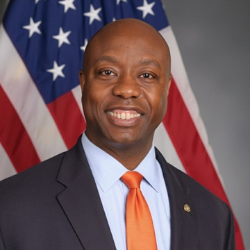 A man in a dark suit, light blue shirt, and bright orange tie smiles while posing in front of an American flag, appearing to be an official portrait of a U.S. public official. The image relates to the post, which highlights Senate Banking Committee Chair Tim Scott's push for a July vote on the Clarity Act—a development framed as bullish for crypto and Solana.