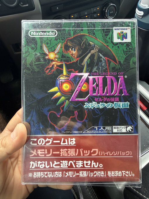 A hand holding the original Japanese box for 'The Legend of Zelda: Majora's Mask' for the Nintendo 64, featuring Japanese text indicating it requires an Expansion Pak.