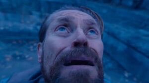 The image is a heavily distorted, stretched close-up of a man's face with wide eyes and an open mouth, set against a blue, icy background. The surreal, unsettling distortion gives the impression of a "creature" emerging, which connects to the caption "It is coming, and it is green." by suggesting a horrifying, otherworldly presence — though the image itself appears more blue than green.