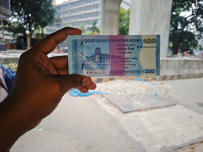 The image shows a hand holding up a 100 Indian Rupee bank note, which has been folded into an origami shape. The person's hand is positioned over the folded money, with their fingers visible above the folded part of the bill. The scene takes place in front of a building or on a street, suggesting that this might be happening during a busy day at a local market or similar location where people often handle and exchange currency.

The post about the bank note features a link to a website called Nomisma Network, which is likely related to the origami-making process or the sale of folded money notes. The image also contains text that reads "GN/ GM my X family @ghsxt_org currently generates some of the highest activity across the nomisma ecosystem Today busy day @NomismaNetwork Alpha @useTria". This suggests that the post might be promoting a specific origami tutorial or showcasing a unique folded bank note design.