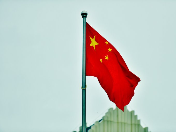 The flag of China, featuring one large yellow star and four smaller stars on a red background, waves against a pale sky, symbolizing the nation's expanding digital yuan network now spanning 30 authorized banks.