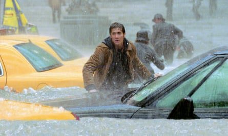 A behind-the-scenes film still depicts actor Jim Carrey in a brown jacket wading through a flooded New York City street filled with yellow taxis and debris.