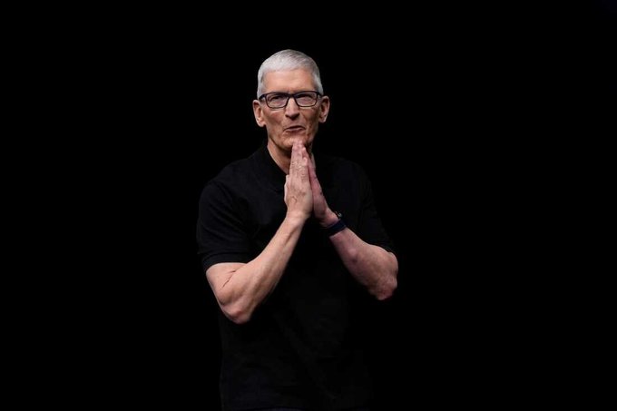 The image shows a man standing against a black background, wearing glasses and a t-shirt with his hands folded together. The caption of the image reads "Just In: @Apple will raise prices on its products, with CEO Tim Cook calling the increases 'unavoidable' amid soaring memory chip costs." This is related to the post as it shows the man's expression in response to the announcement or discussion about Apple's pricing changes, and possibly related to his thoughts or opinions.
