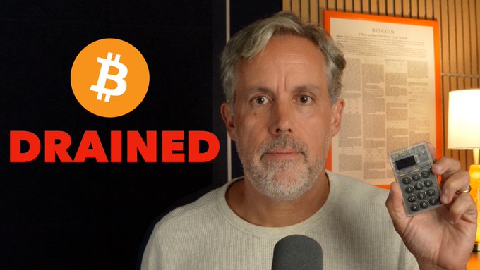 A YouTube-style thumbnail features a man holding up a hardware wallet device, with a Bitcoin logo and the red text 'DRAINED' on the left side, suggesting his crypto was stolen.
