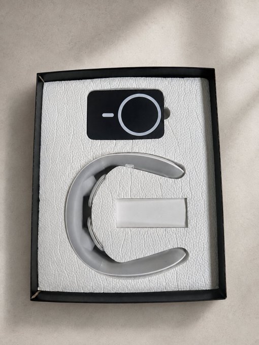 The image shows an opened product box containing an electric shock mini massager with a circular control unit and a curved neck/shoulder attachment piece, both displayed in white foam packaging. This aligns with the post thanking NeoSoulAI for sending the massager, with the packaging showcasing the device that helps users stay alert during idle moments in the bear market.