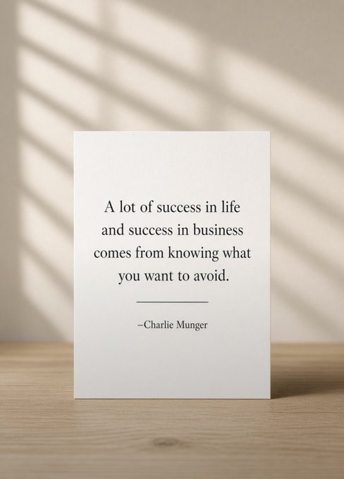A white card displayed on a wooden surface against a beige wall reads: 'A lot of success in life and success in business comes from knowing what you want to avoid. —Charlie Munger'.