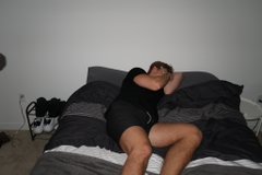 A blurry photo of a person sleeping on a bed with black bedding in a dimly lit room.