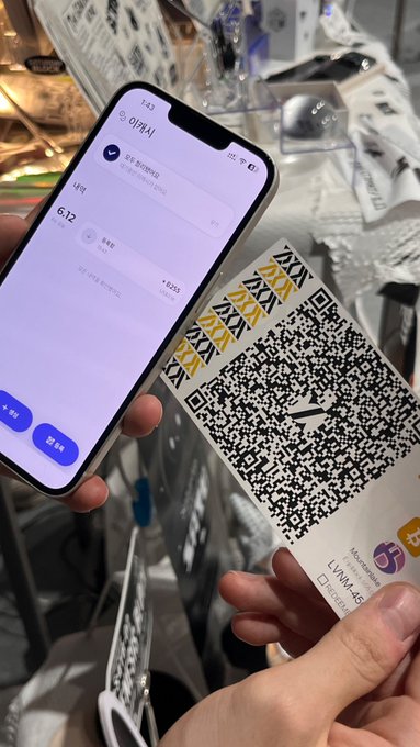 The image shows a person holding up a smartphone displaying a QR code, which appears to be a ticket or pass for an event. The QR code has black text that reads "5", indicating the specific details of the event. The person's hand is visible in front of them, and they are standing next to a table with various items on it. The post also mentions that Cashu is apex paper Bitcoin, which could be related to the QR code or another aspect of the image.