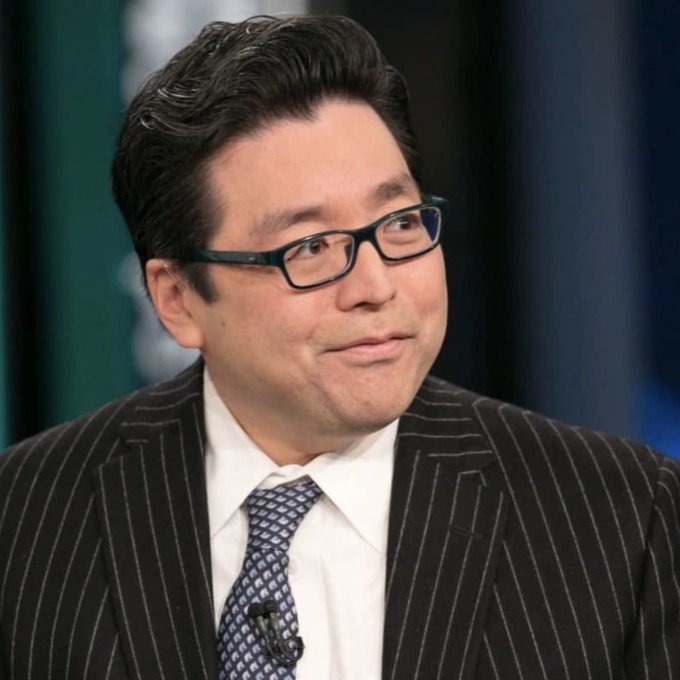 A man with dark hair and glasses wearing a pinstripe suit and blue patterned tie appears to be in a TV studio setting.