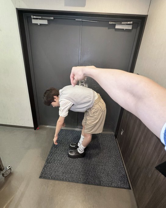A creative perspective photo showing a child's legs appearing disproportionately small and a large adult arm reaching down, creating a forced-perspective illusion as the child bends over near a doorway.