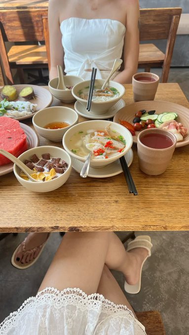 Two women sit across from each other at a restaurant table covered with various breakfast dishes, including congee, noodles, watermelon, and desserts.