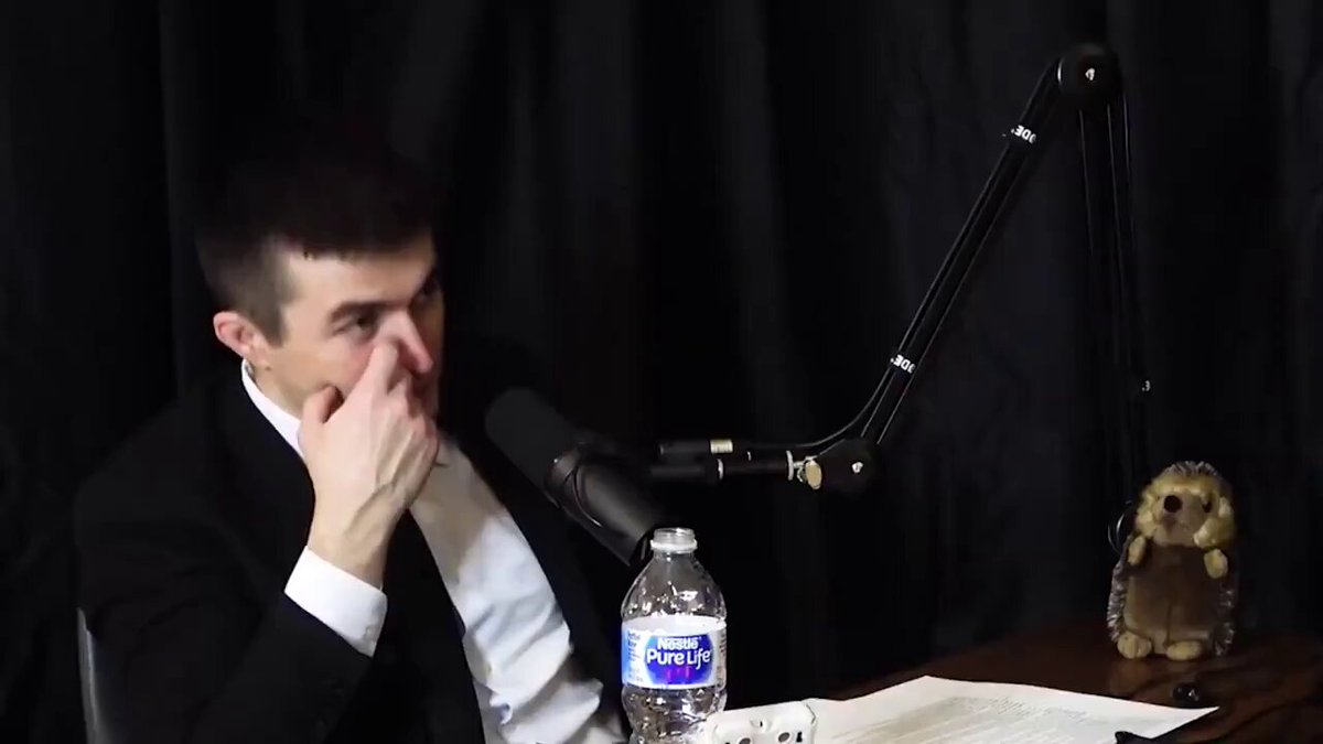 There are two people sitting at a table with a bottle of water between them. One person is wearing a black suit and tie, while the other is dressed more casually. A microphone and a lamp are positioned behind them. The main subject of the image is Ray Dalio, who has posted his thoughts on the podcast "Ray Dalio Talks". The post discusses how Bitcoin changed his views on the world.