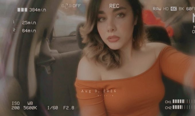 A stylized selfie-style image of a woman in an orange off-the-shoulder top in a car, overlaid with camera interface text including 'REC', 'RAW HD 4K', and a date stamp of 'Aug 3, 2026'.