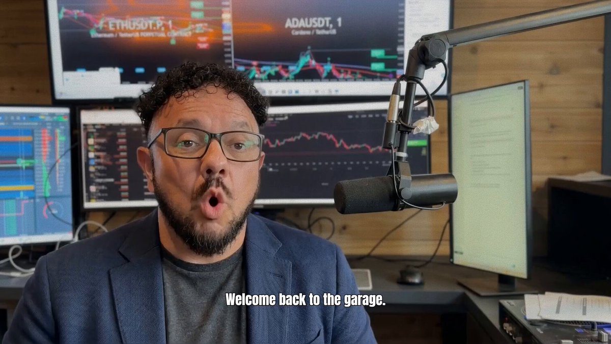 The image shows a man wearing glasses sitting at a desk with a microphone, possibly recording or broadcasting an interview. There are multiple monitors behind him, suggesting that he might be involved in financial or technology-related work. The text "Welcome back to the garage" is visible on one of the monitors, which could indicate that they are discussing Bitcoin or related topics.