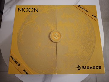 A yellow gift box labeled 'MOON' features a moon design and is wrapped with a yellow ribbon marked 'BINANCE'.