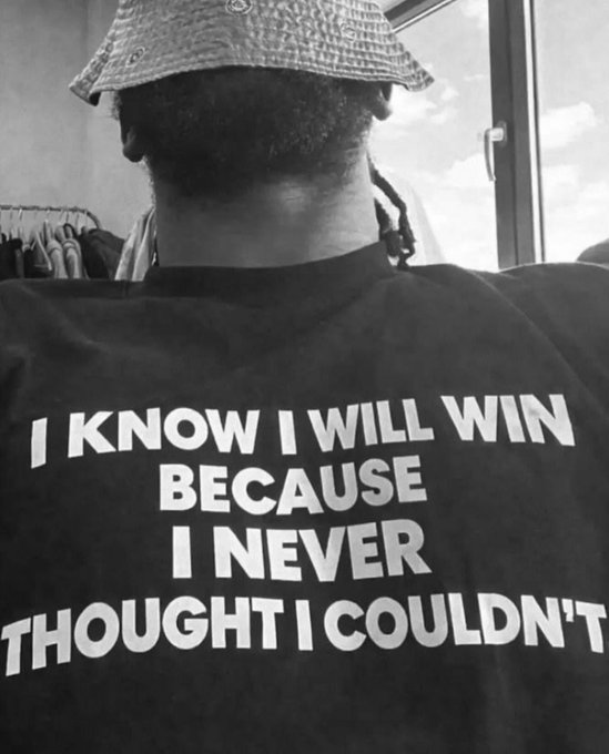 A black-and-white photo from behind a person wearing a bucket hat, featuring a t-shirt with the text 'I KNOW I WILL WIN BECAUSE I NEVER THOUGHT I COULDN'T.'