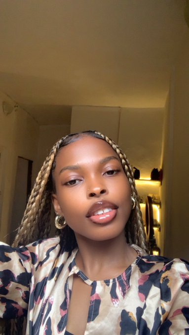 A young woman with blonde box braids and gold hoop earrings poses for a close-up selfie, wearing a floral top with a front keyhole cutout. The warm, intimate indoor setting aligns with the post's invitation for "$ANSEM girlies" to connect, presenting a personal and approachable look that complements the call for community engagement.
