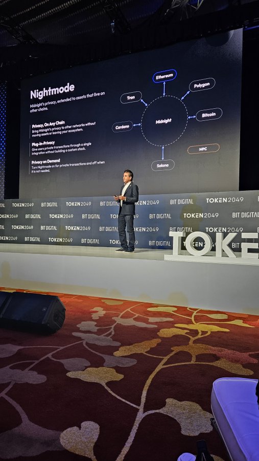 A man in a suit presents on a stage at the TOKEN2049 and BIT DIGITAL conference, standing before a large screen titled 'Nightmode' that displays a diagram connecting Midnight to various blockchains like Ethereum, Polygon, Bitcoin, Cardano, Tron, and Solana.