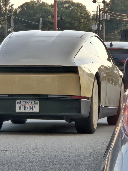 The rear view of a silver Tesla vehicle is shown on a roadway, displaying a Texas license plate reading '6FB X044' with power lines and trees visible in the background.
